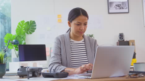 Architektin-Im-Büro-Am-Schreibtisch-Mit-Drohne,-Die-Mit-Laptop-An-Plänen-Für-Ein-Neues-Gebäude-Arbeitet