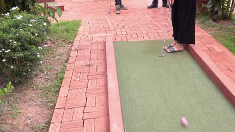 person setting up the ball and teeing off at the mini golf