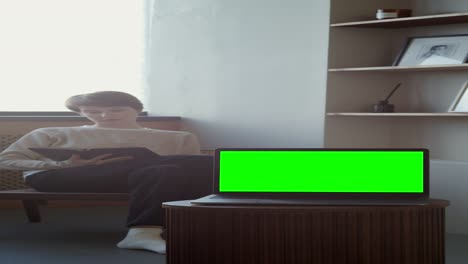 woman reading a book while working on laptop at home