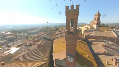 Drone-Volando-Sobre-Edificios-Con-Techo-De-Tejas-Hacia-Palazzo-Pretorio-Con-La-Iglesia-De-San-Martino-En-El-Fondo-En-Sinalunga,-Siena,-Italia