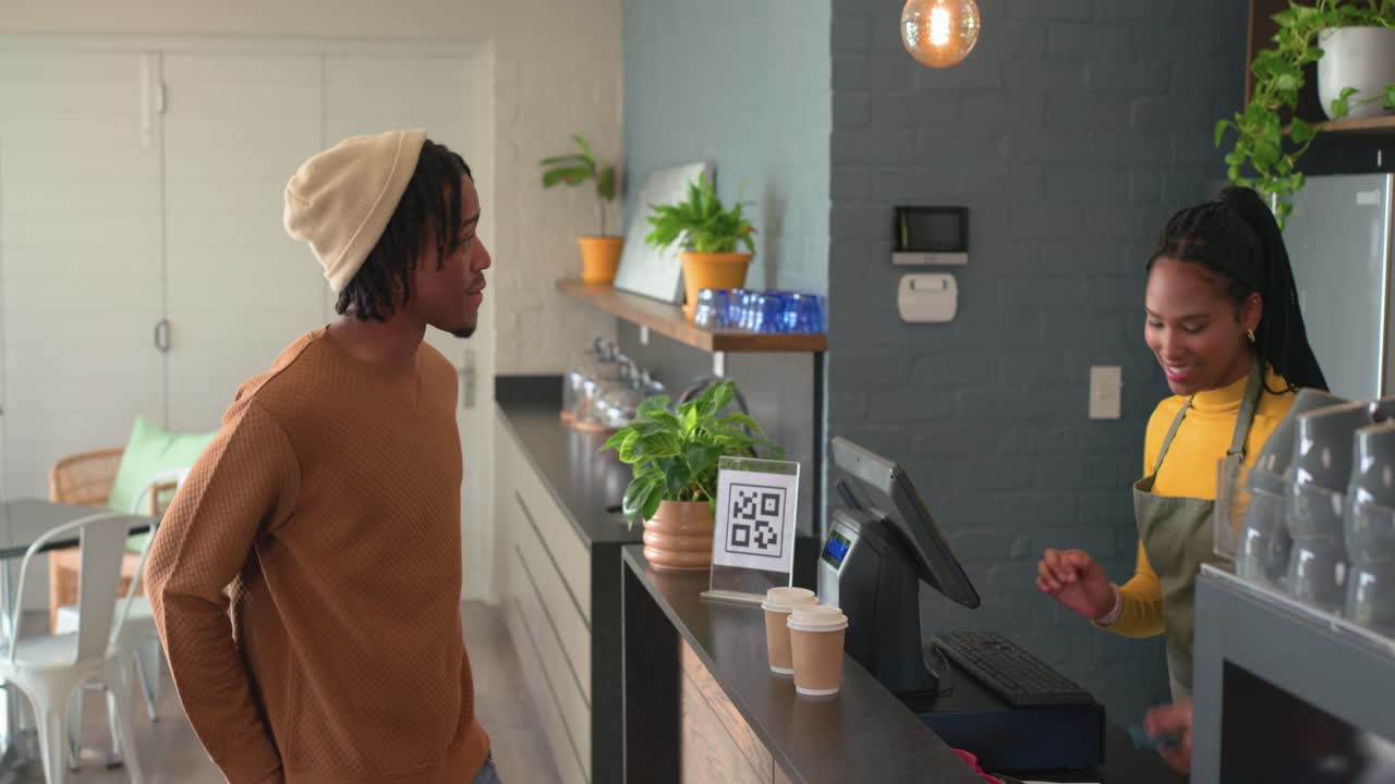 Afro-americano entrando em cafeteria, mexendo no celular, passando o cartão e pegando copos para viagem