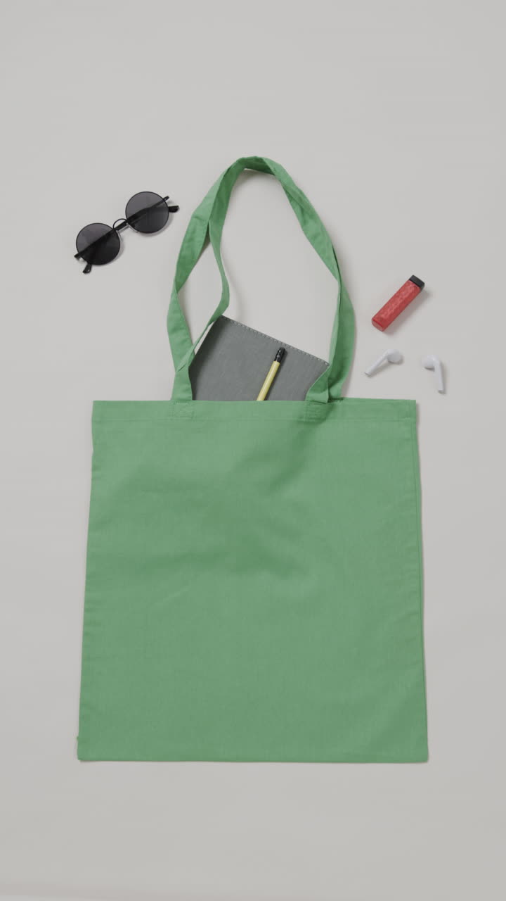 Vertical video of green bag with sunglasses, notebook and lipstick, copy space, slow motion