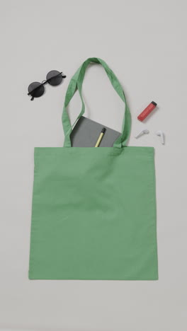 vertical video of green bag with sunglasses, notebook and lipstick, copy space, slow motion
