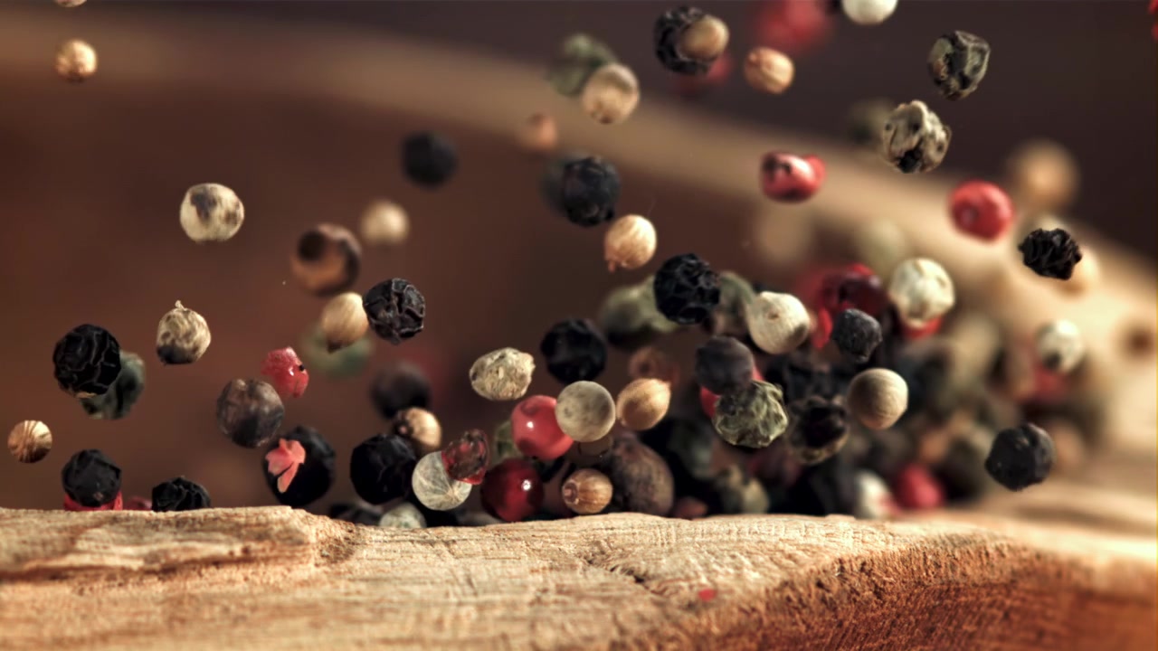Mixed Peppercorns Falling in Slow Motion onto a Rustic Wooden Surface