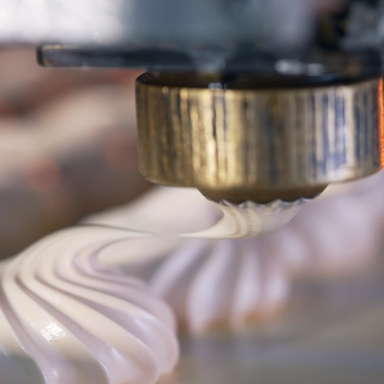 Un piccolo ugello rotante rilascia una sostanza cremosa su un nastro trasportatore. Primo piano. I dessert alla vaniglia vengono spremuti a poca distanza l'uno dall'altro. Produzione di dolciumi in una fabbrica di pasticceria