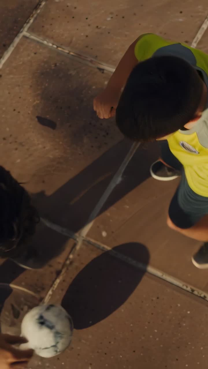 Video verticale: Mano che tocca l'inizio del lancio, uomo che guida un ragazzo a giocare a passaggi nel patio con una palla.
