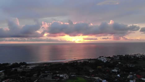 Toma-Aérea-De-Establecimiento-De-Una-Puesta-De-Sol-Rosa-Dorada-Sobre-El-Océano-En-Bali-Indonesia