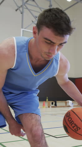 vertical video of male caucasian basketball player training in indoor court, in slow motion