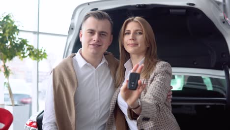 happy couple showing keys of his new car in dealership. auto business, car sale