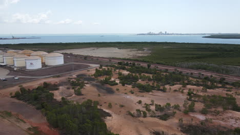 Descending-Aerial-Drone-shot-of-East-Arm-Industrial-Area-and-Oil-Storage-with-Darwin-Skyline,-Northern-Territory