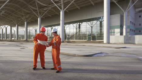 trabajadores de la construcción en uniforme naranja y cascos duros mirando los planes juntos. edificio en el fondo