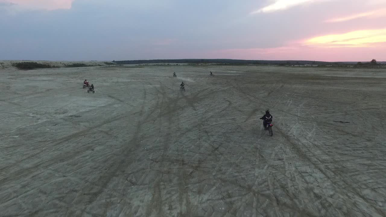 motociclistas montando bicicletas de tierra en un paisaje desértico al atardecer