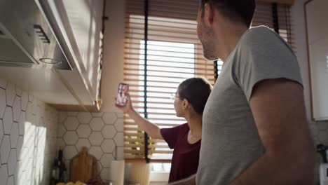 Caucasian-teenager-girl-and-her-father-having-video-call-with-mother-while-cooking