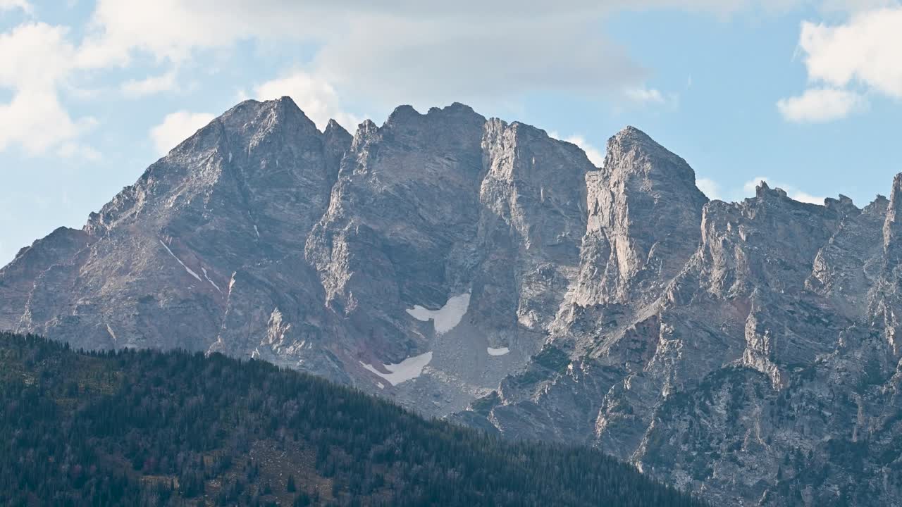 Puncak gunung yang menjulang tinggi di Taman Nasional Grand Teton dengan tebing terjal dan langit biru di atasnya.
