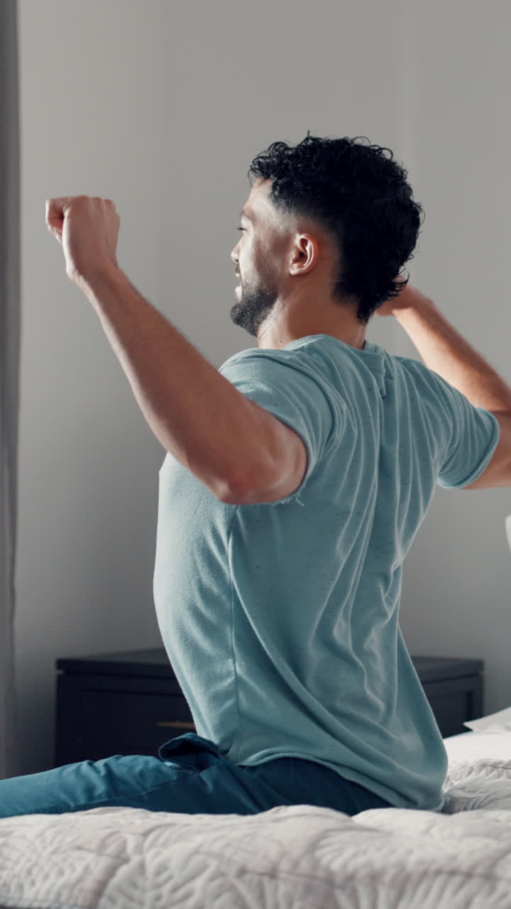 Giovane uomo che si allunga e si sveglia a letto al mattino