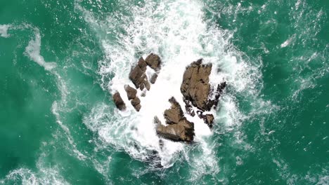 Toma-Aérea-Ascendente-De-Arriba-Hacia-Abajo-De-Olas-Rompiendo-En-Rocas-Gigantes-En-Un-Océano-Claro-En-Nueva-Zelanda