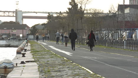 Menschen,-Die-Bei-Sonnenuntergang-In-Der-Nähe-Der-Brücke-Des-25.-April-Am-Tejo-Spazieren-Gehen