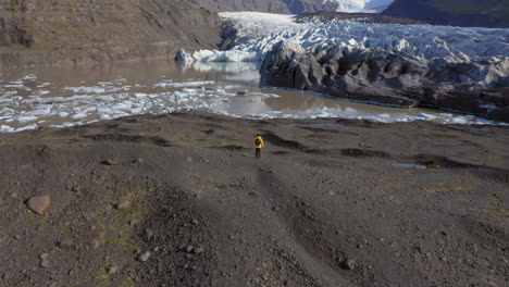 Antena:-Toma-Panorámica-Lenta-De-Un-Hombre-Parado-En-Una-Colina-Cerca-Del-Glaciar-Svinafellsjokull-Durante-Un-Día-Soleado