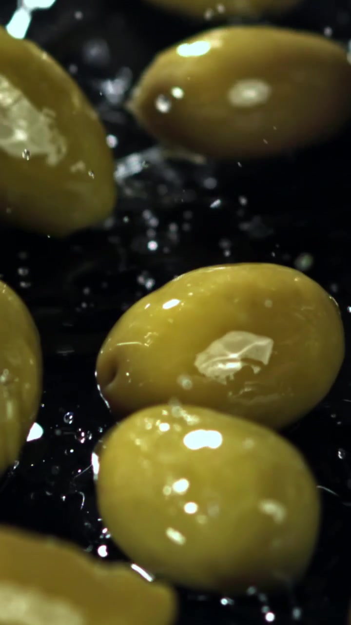 Olive verdi fresche che cadono e schizzano nell'acqua al rallentatore