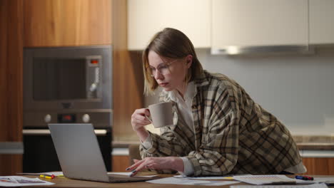 Una-Mujer-Bebe-Café-Y-Mira-Su-Computadora-Portátil-Mirando-Los-Documentos