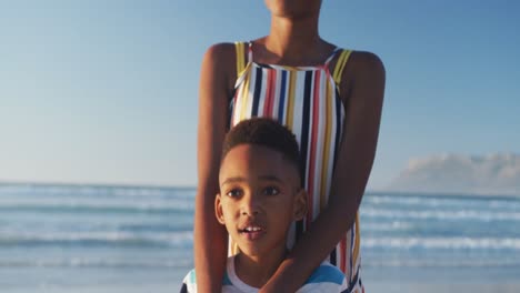 Feliz-Madre-Afroamericana-Abrazando-A-Su-Hijo-En-La-Playa-Soleada