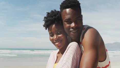 portrait of happy african american couple embracing on sunny beach