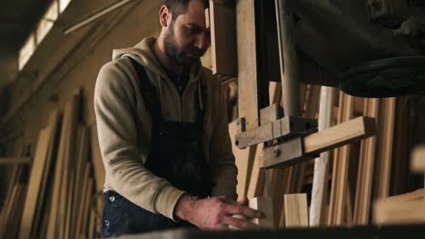 El-Joven-Carpintero-Está-Extremadamente-Concentrado-Trabajando-Con-La-Sierra-Eléctrica.-Funciona-Con-Barras-Pequeñas.-Madera-En-El-Fondo