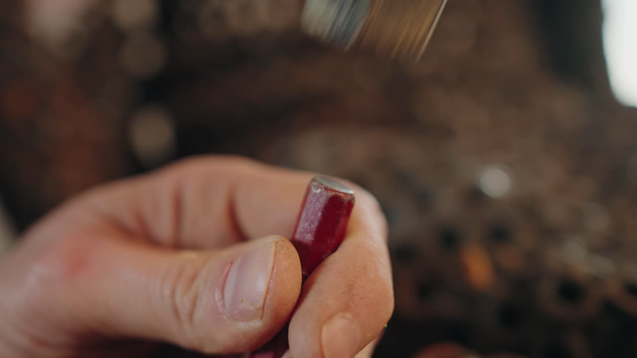 close up of hammer hitting red rod held by hand in warm workshop light