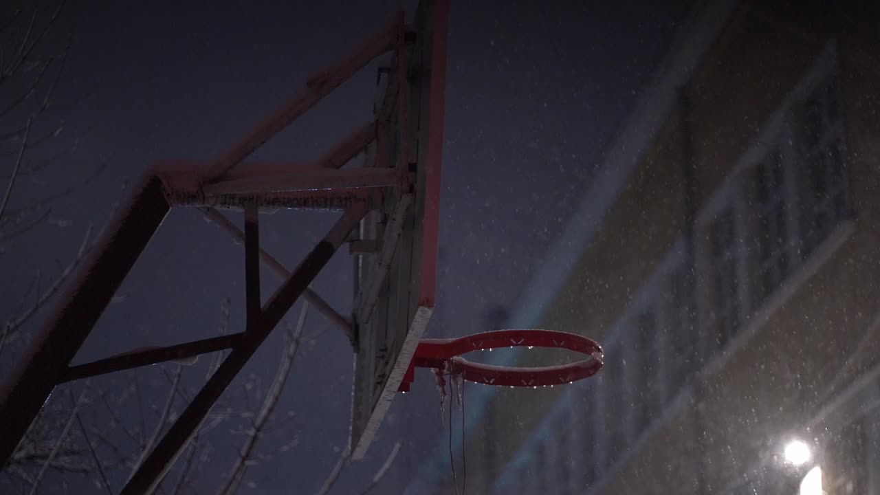 la nieve cae alrededor del tablero y el borde del baloncesto sin red por la noche