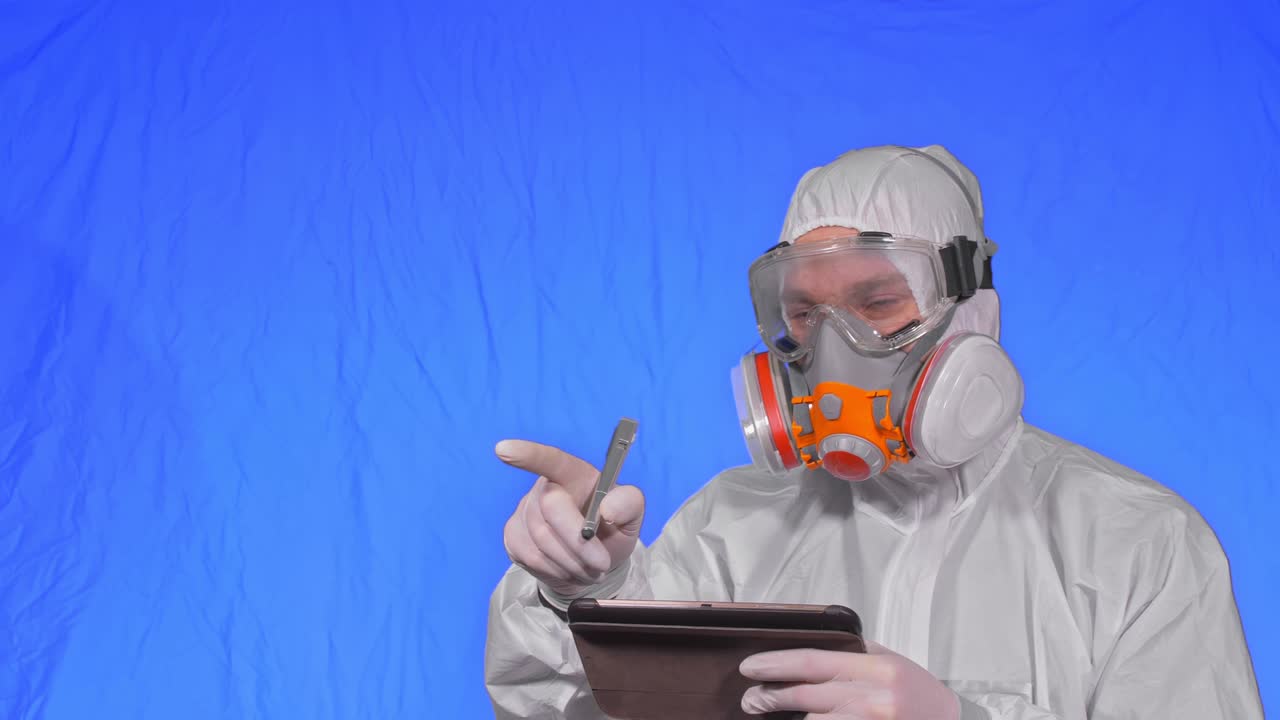 인공호흡기에서 바이러스학자 과학자는 태블릿 컴퓨터에 스타일러스를 사용하여 글을 쓴다. 보호 의료 마스크를 착용한 남자. 크로마 키 파란색.