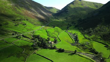 Mountain-pass-winding-through-lush-green-countryside-towards-steep-mountains-on-summer-day