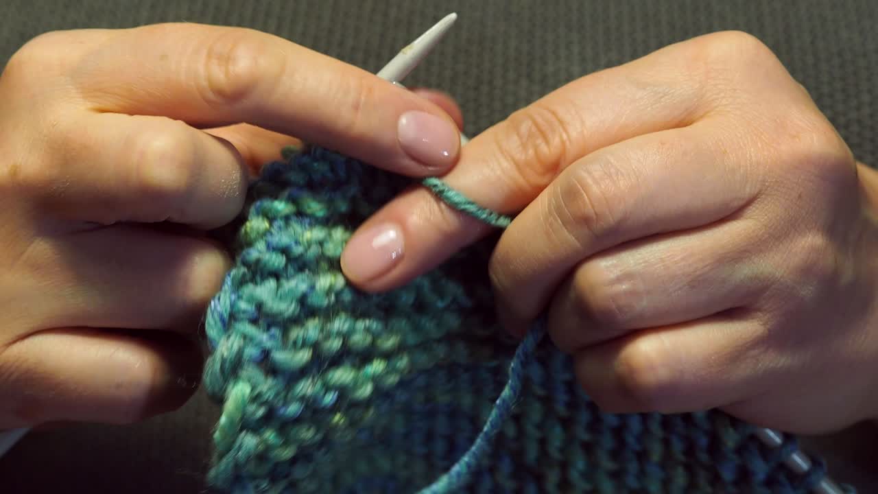 여성의 손은 따뜻한 전기 조명 아래 스카프를 뜨개질합니다.