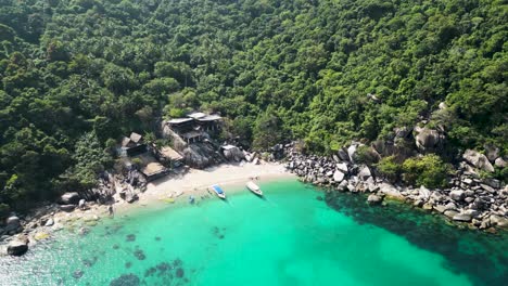 Cabañas-Junto-Al-Mar-Con-Barcos-En-Una-Ensenada-En-La-Bahía-De-Mango,-Isla-De-Ko-Tao,-Tailandia,-Con-Turistas-En-La-Playa,-Tiro-De-Aproximación-De-Descenso-Aéreo