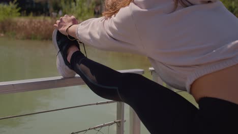 chica con pantalones de yoga estirando las piernas después de trotar al sol de la mañana