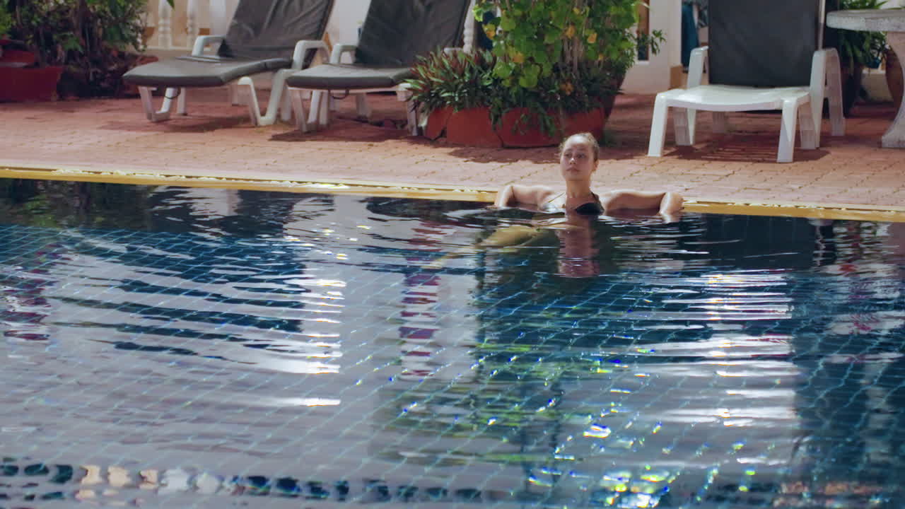 Hvid mand træner i ø-pool, morgensol på fliser, træder vande nær poolkanten, livlige krusninger og plask, liggestole og tropiske planter på hotelterrasse, munter feriefitness.