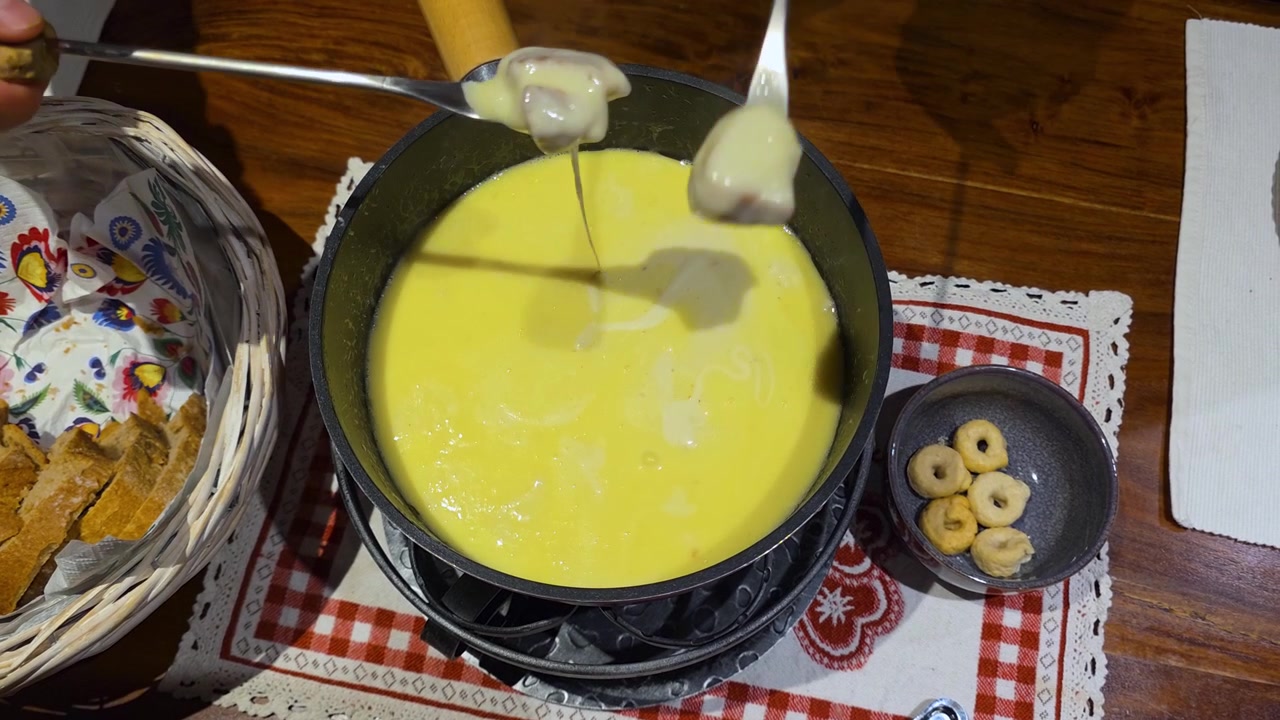 Gros plan sur des mains trempant du pain dans un caquelon bouillonnant de fondue au fromage suisse authentique. Parfait pour le contenu culinaire, hôtelier et de repas à domicile.