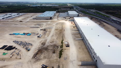 an aerial shot captures the construction of a large industrial building near a highway, showcasing the ongoing work.