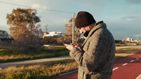 old man scrolling his smartphone under the winter sun