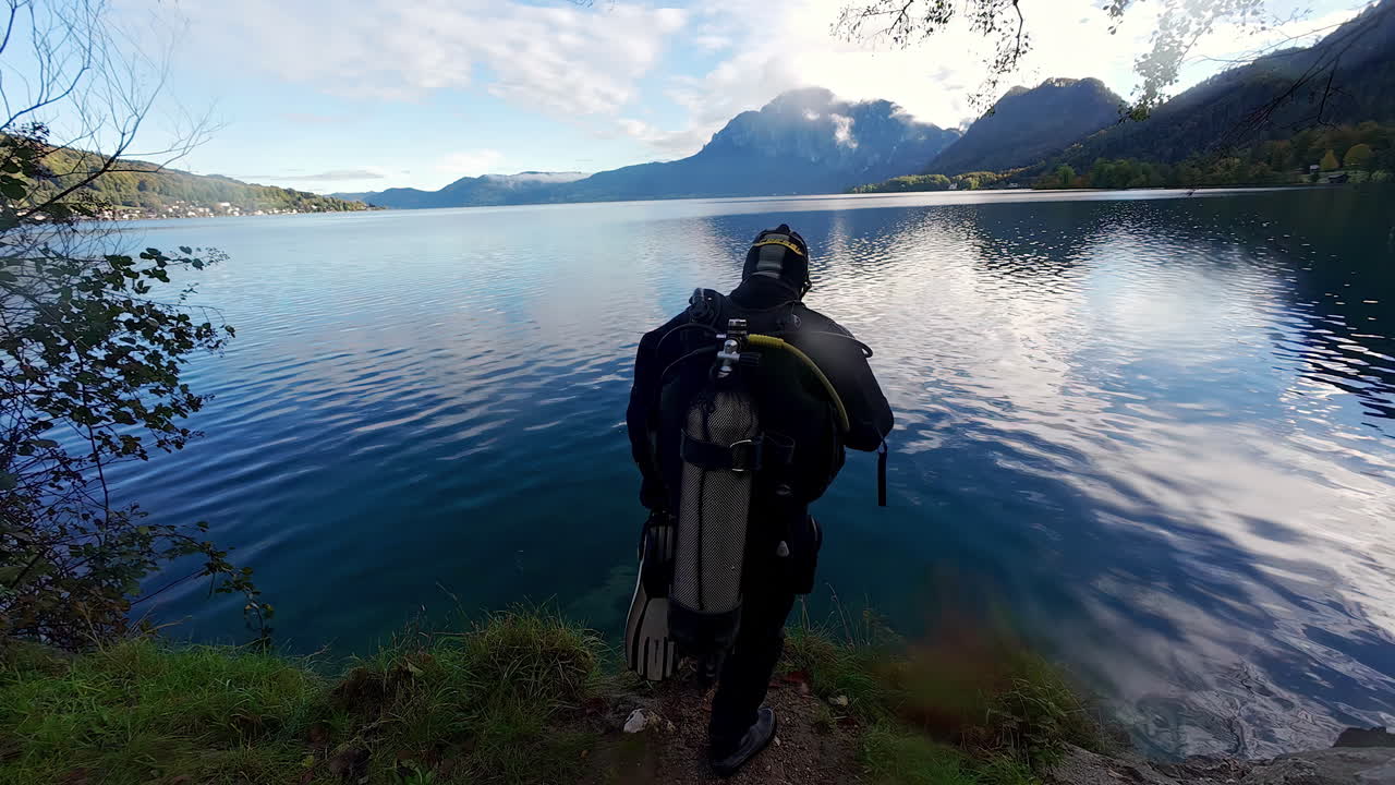 un buzo se prepara y salta a un hermoso lago con montañas en el fondo