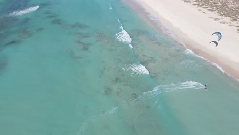 Sobrevuelo-Aéreo-Océano-Cristalino-Con-Dos-Kitesurfistas-Cruzando-Divirtiéndose-Durante-El-Día-Ventoso-Y-Soleado-En-Australia-En-La-Vista-Superior