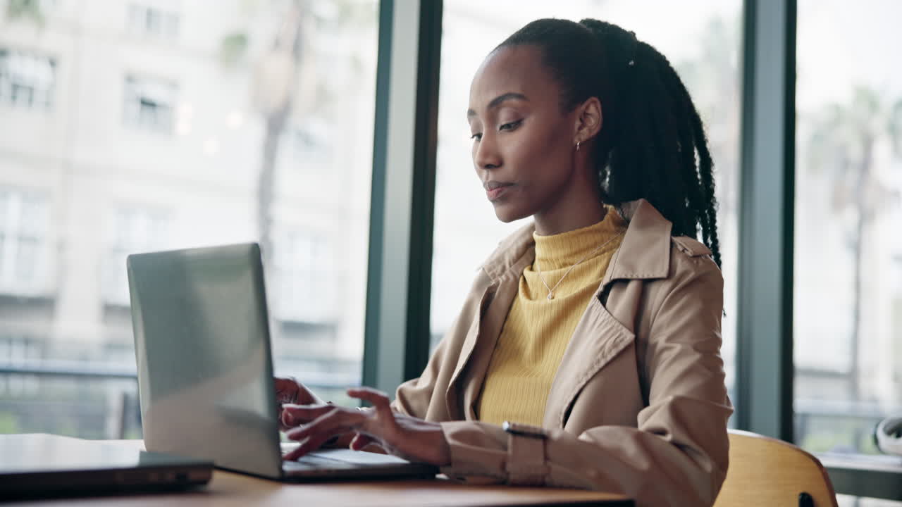 Serious black woman typing on laptop in cafe
