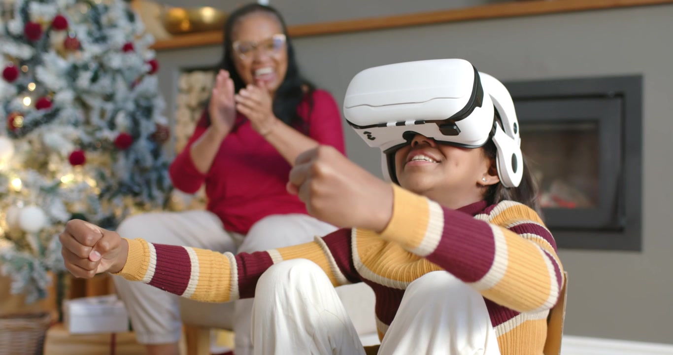 Famiglia femminile afroamericana, la giovane che posiziona il visore VR, il controller, l'anziana che applaude incoraggiando.