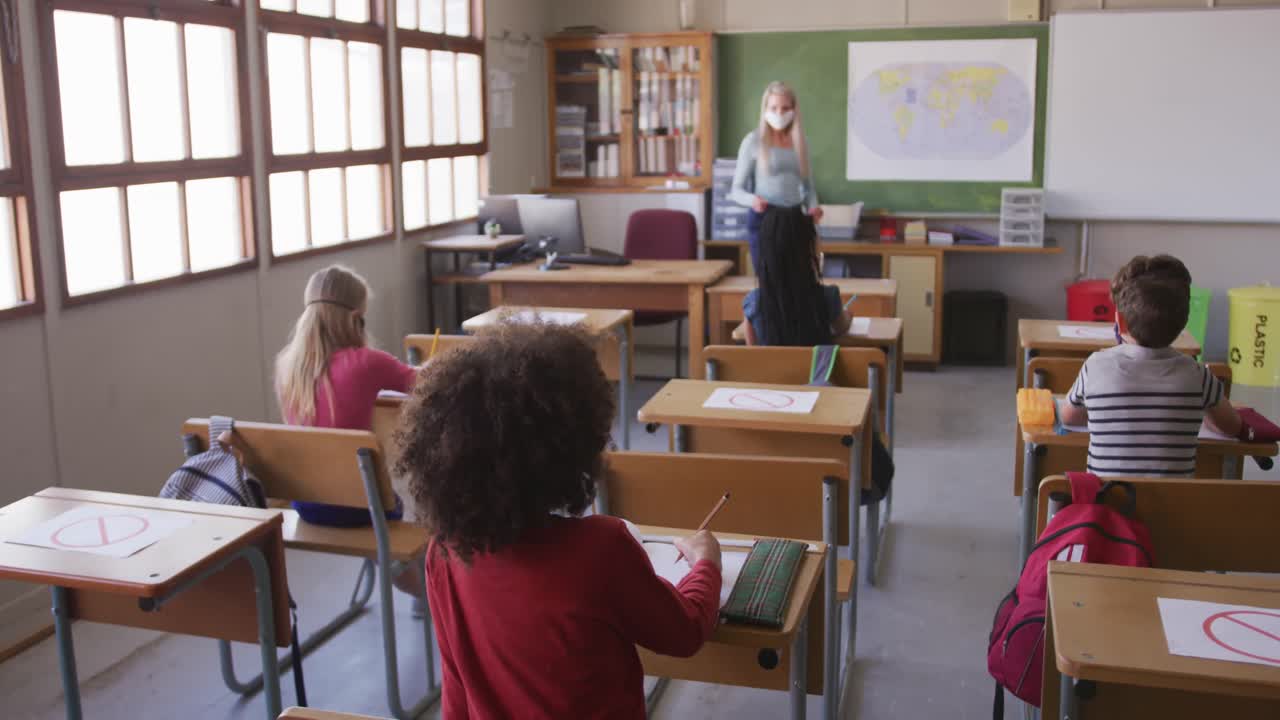 grupo de niños con máscaras faciales levantando las manos en la clase en la escuela