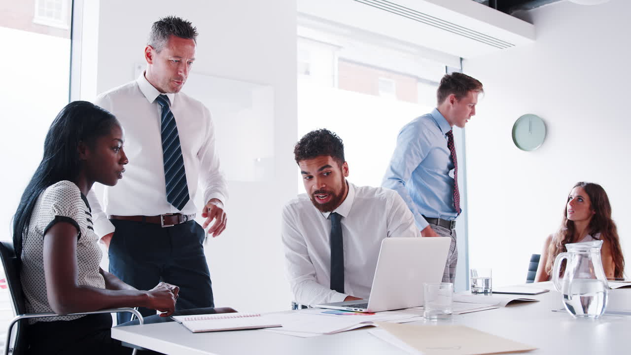 Slow Motion Shot Of Businessmen And Businesswomen Meeting Around Table In Modern Boardroom Working On Laptop Together