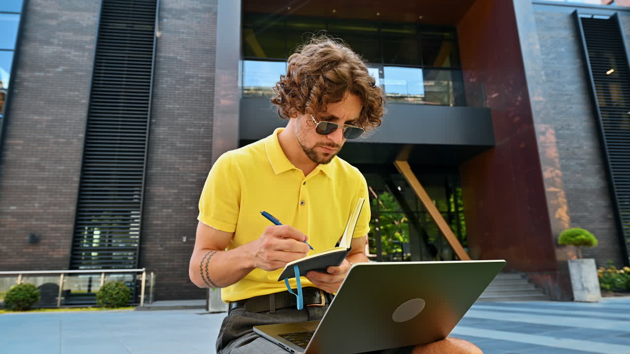 Man in yellow shirt talking standing on a bench and writing in a notebook