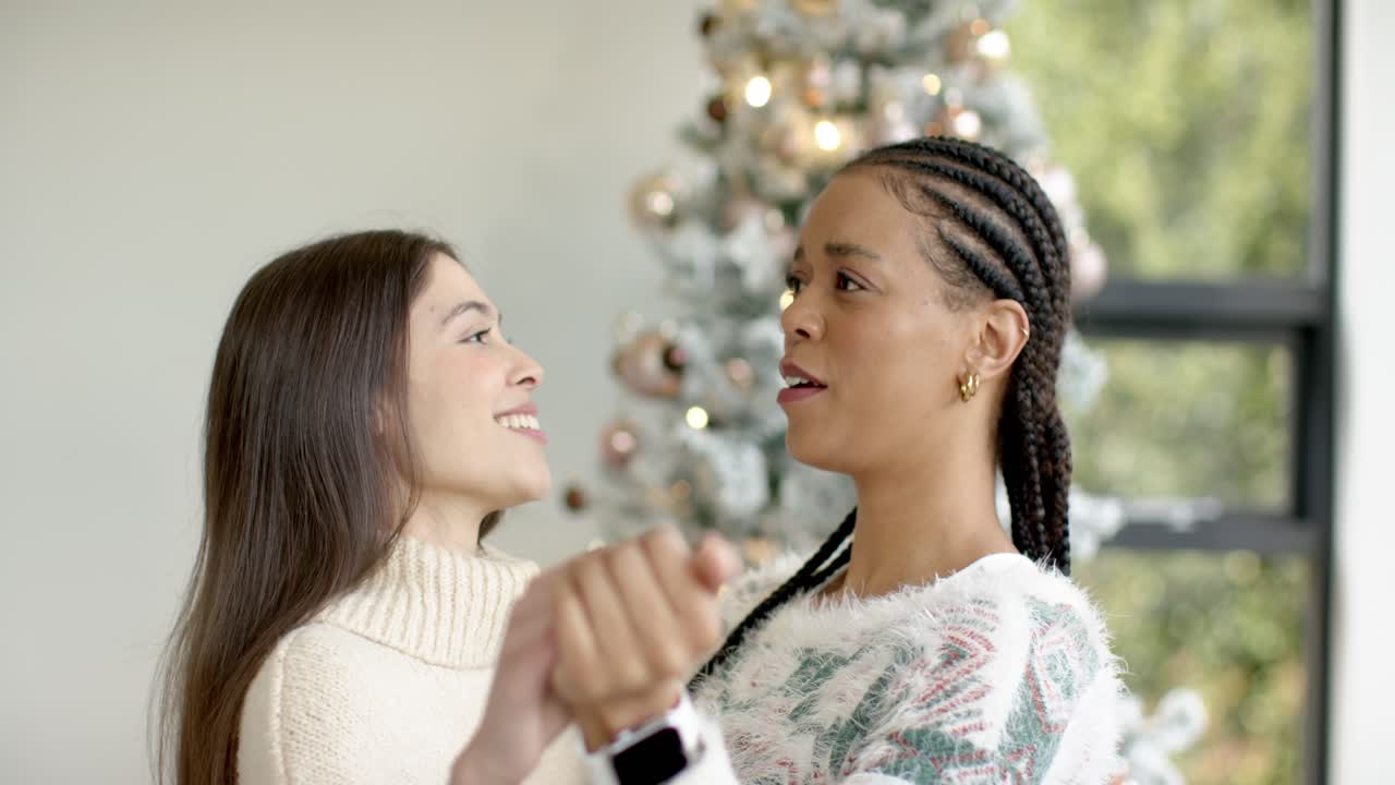 Diversas parceiras alcançando as mãos e dançando perto da árvore de Natal, celebrando a alegria das festas