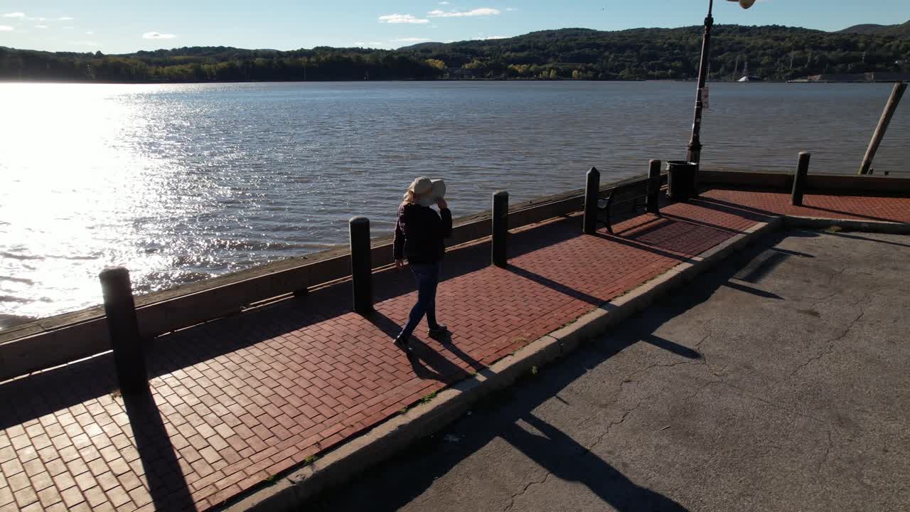 A woman walks along a brick paved, boat dock in upstate, NY on a sunny morning