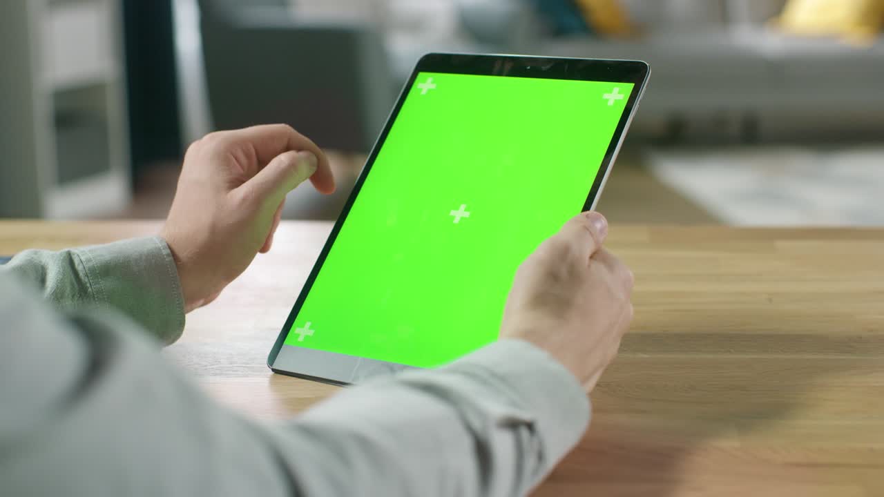 hombre usando gestos de la mano en pantalla de maqueta verde computadora tableta digital en modo retrato mientras está sentado en su escritorio. en el fondo acogedor salón.