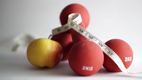 apple rolls into two crossed red dumbbells on a white background, slomo