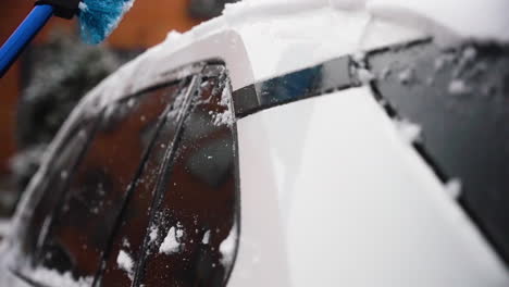 person using a handle brush to wipe snow from the car side panel during detailed cleaning work as they get ready for the day